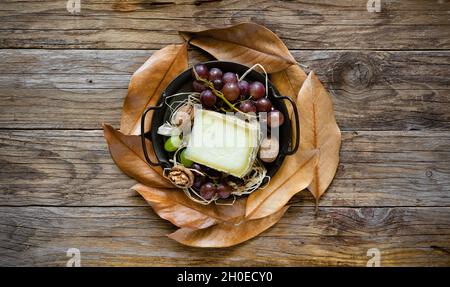 fetta di pecorino con fieno di montagna, su sfondo autunnale con uve nere Foto Stock