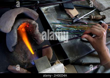 Le mani di un lavoratore di fiamma durante la fabbricazione di perle di vetro. Questa arte è stata iscritta nel 2020 sulla lista rappresentativa del patrimonio culturale immateriale Foto Stock