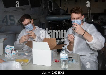 OKINAWA, Giappone (Feb 14, 2021) Hospital Corpsmen Dillon Bothell, Left e Devin Declercq preparare i colpi di vaccinazione COVID-19 a bordo della nave portuale di trasporto anfibio USS New Orleans (LPD 18). New Orleans, parte dell'America Expeditionary Strike Group, insieme alla 31st Marine Expeditionary Unit, sta operando nell'area di responsabilità della 7th Fleet statunitense per migliorare l'interoperabilità con alleati e partner e fungere da forza di risposta pronta per difendere la pace e la stabilità nella regione indopacifica. Foto Stock