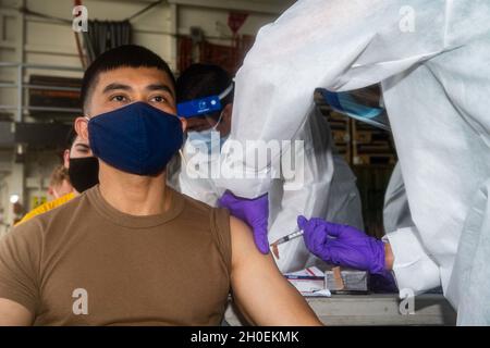 OKINAWA, Giappone (Feb 14, 2021) Aviation Boatswain's Mate (Handling) 1st Class Timmy Vu, di Santa Ana, California, riceve un vaccino COVID-19 a bordo di una nave portuale di trasporto anfibio USS New Orleans (LPD 18). New Orleans, parte dell'America Expeditionary Strike Group, insieme alla 31st Marine Expeditionary Unit, sta operando nell'area di responsabilità della 7th Fleet statunitense per migliorare l'interoperabilità con alleati e partner e fungere da forza di risposta pronta per difendere la pace e la stabilità nella regione indopacifica. Foto Stock