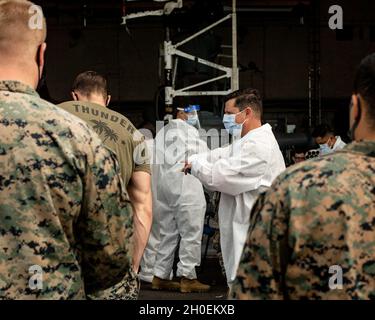 Marines e marinai statunitensi con la 31esima unità Marine Expeditionary (MEU), si preparano a ricevere e somministrare la prima vaccinazione COVID-19 a bordo della USS New Orleans (LPD 18), a Okinawa, Giappone, 14 febbraio 2021. Il 31 MEU opera a bordo di navi dell'America Expeditionary Strike Group nella settima area di attività della flotta per migliorare l'interoperabilità con gli alleati e i partner e fungere da pronta forza di reazione per difendere la pace e la stabilità nella regione IndoPacifico. Foto Stock