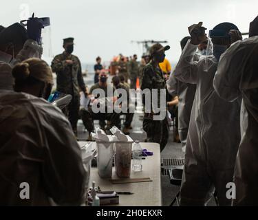 Marines e marinai statunitensi con la 31esima unità Marine Expeditionary (MEU), si preparano a ricevere e somministrare la prima vaccinazione COVID-19 a bordo della USS New Orleans (LPD 18), a Okinawa, Giappone, 14 febbraio 2021. Il 31 MEU opera a bordo di navi dell'America Expeditionary Strike Group nella settima area di attività della flotta per migliorare l'interoperabilità con gli alleati e i partner e fungere da pronta forza di reazione per difendere la pace e la stabilità nella regione IndoPacifico. Foto Stock