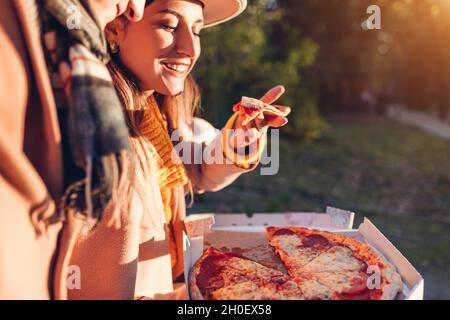 Coppia amorevole che ha una pizza pepperoni nel parco autunnale. Donna e uomo gustare cibo gustoso all'aperto. Mangiare uno spuntino caldo Foto Stock