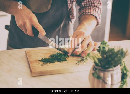 Primo piano della mano del maschio che taglia l'aneto fresco su asse di legno in cucina nel paese Foto Stock