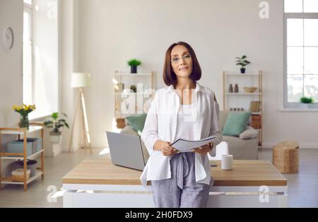Ritratto di elegante donna d'affari adulta in piedi accanto alla scrivania nel suo ufficio a casa Foto Stock