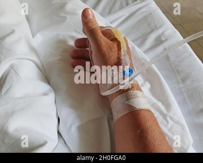 Catetere venoso periferico nella vena della mano umana. Terapia medica e aiuto per la persona che si trova nel letto della stanza dell'ospedale. Foto Stock