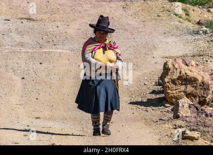 Una donna peruviana nativa che si inginocchiava mentre camminava su una strada sterrata. Perù, Sud America. Foto Stock