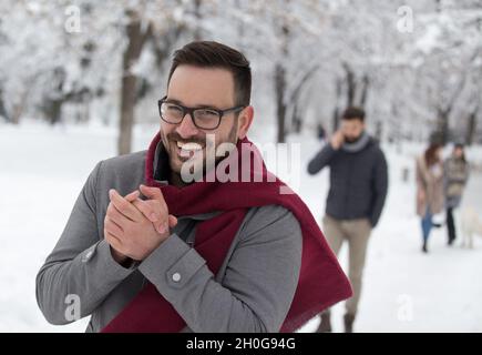 Uomo che gela sulla neve, soffia le mani nella foresta Foto Stock
