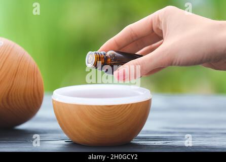 Donna che aggiunge olio essenziale al diffusore di aroma sul tavolo Foto Stock