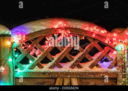 Decorazioni natalizie, neve, recinzione in legno, luci multicolore che illuminano, da vicino Foto Stock