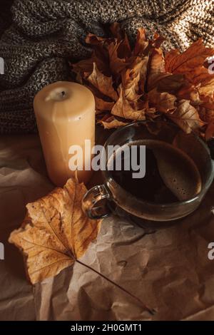 Candela gialla e grande tazza di caffè nero in una casa accogliente autunno sera ancora vita. Tonalità arancio calde. Scatto verticale Foto Stock