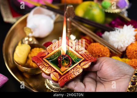 Mani di ragazza in Bangles che tiene Clay Diya Deep dia lampada illuminata con Pooja Thali, Fiori, Mithai, Agarbatti e fare Aarti. Diwali Puja , New Y Foto Stock