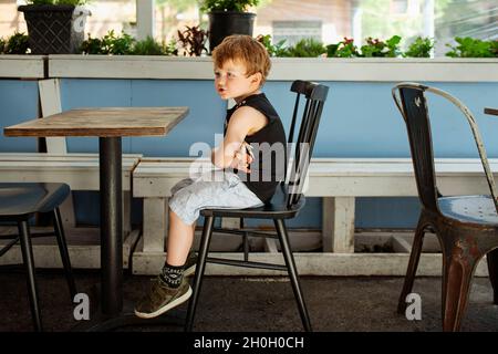 Cena all'aperto durante il Covid 19. Un ragazzino seduto ad un tavolo vuoto in un ristorante di New York City. Foto Stock