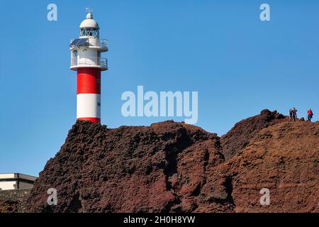 Faro rosso e bianco sulla costa rocciosa, i visitatori godono di vista, Punta de Teno, Buenavista del Norte, Tenerife, Spagna Foto Stock
