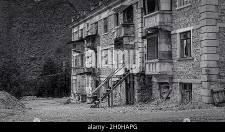 Foto in bianco e nero di vecchio edificio abbandonato parzialmente crollato con intricati lavori in pietra, balconi in rovina, finestre schiantate. Desolazione e. Foto Stock