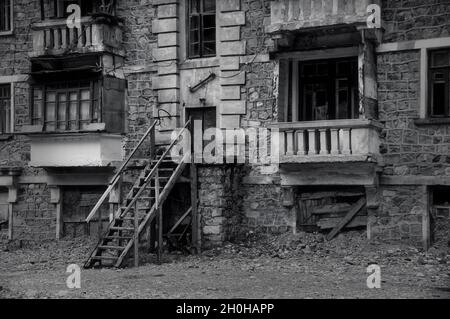 Foto in bianco e nero di vecchio edificio abbandonato parzialmente crollato con intricati lavori in pietra, balconi in rovina, finestre schiantate. Desolazione e. Foto Stock