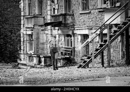 SADON, RUSSIA - 07 25 2021: Straniero solitario esitante a fare un passo avanti su un territorio desolato accanto a vecchio edificio abbandonato parzialmente crollato con Foto Stock