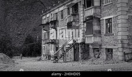 SADON, RUSSIA - 07 25 2021: Vecchio edificio abbandonato con intricati lavori in pietra, balconi rovinati, finestre schiantate e uno straniero solitario lontano sullo sfondo Foto Stock