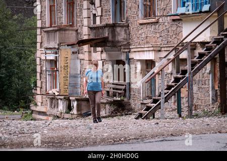 SADON, RUSSIA - 07 25 2021: Straniero solitario esitante a fare un passo avanti su un territorio desolato accanto a vecchio edificio abbandonato parzialmente crollato con Foto Stock