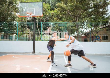 un giocatore di basket che porta la palla è bloccato dai giocatori del suo avversario Foto Stock