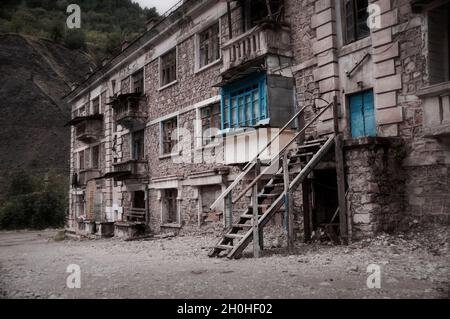 Edificio abbandonato in rovinato dalla città vecchia infangata in alto in montagna con intricati lavori in pietra, balconi in rovina, finestre schiantate. Desolazione e. Foto Stock