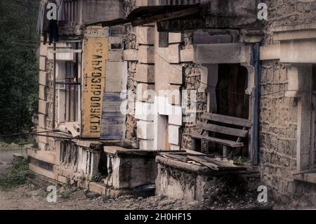 SADON, RUSSIA - 07 25 2021: Vecchio edificio abbandonato in rovinato da fango piccola città alta in montagna con vecchio segno sovietico Grocery Store 2 in russo Foto Stock