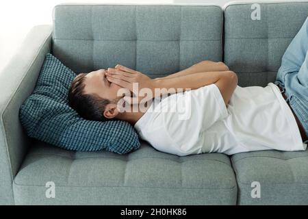 L'uomo depresso sdraiato sul viso di pelle di pianto del divano soffre di dolore, ansia, stress o rottura nervosa Foto Stock