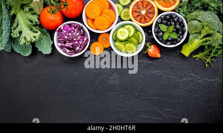 Colorati Frullati salutari e di succhi di frutta in bottiglie con fresca frutta tropicale e superfoods sulla pietra scura con sfondo spazio copia. Foto Stock