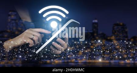 Concetto di wireless Wi Fi. Tablet bianco touch a mano con ologramma digitale Wi Fi segno sulla città scuro sfondo sfocato. Connessione di rete aziendale Foto Stock