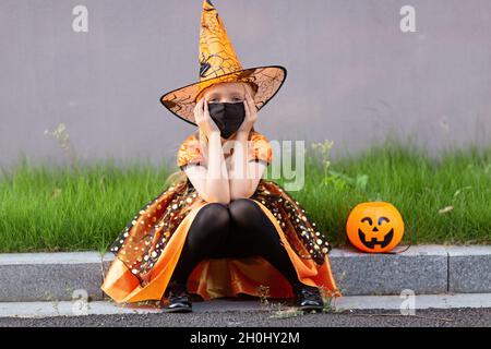 Ritratto lifestyle di ragazza caucasica felice con capelli biondi sette anni in costume arancione nero di cui celebra Halloween da solo Foto Stock