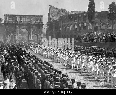 Il Ministro dell'aria Italo Balbo era volato in luglio e agosto in un viaggio di andata e ritorno con uno squadrone di aerei dall'Italia a Chicago e ritorno (la cosiddetta Crociera aerea del Decennale). Il 13 agosto 1933, il giorno dopo il ritorno, l'arrivo dello squadrone di Balbo è stato celebrato a Roma con una grande festa. Nella foto, i piloti e gli equipaggi di volo stanno marciando su Via Celio Vibenna, nell'antica città vecchia di Roma. Sullo sfondo si trova l'Arco di Costantino, con parte del Colosseo visibile a destra. Migliaia di spettatori allineano i sentieri. [traduzione automatizzata] Foto Stock