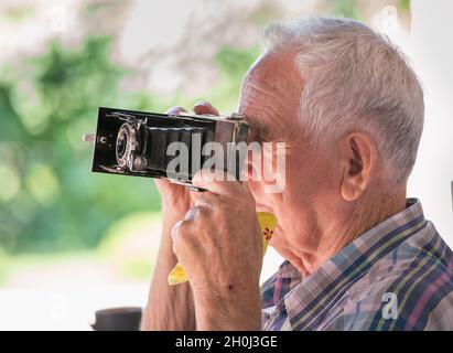 Uomo anziano che scatta foto con la vecchia telecamera analogica nel parco Foto Stock