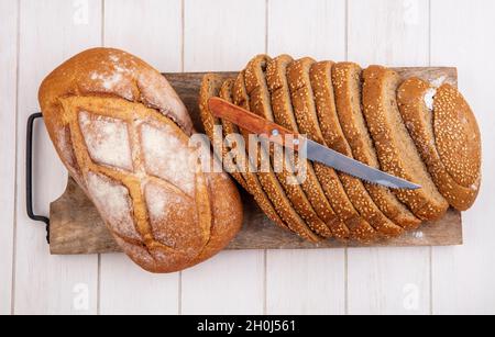 vista dall'alto del pane, come panino bruno seminato e crosty pane affettato con coltello sul tagliere su sfondo di legno Foto Stock