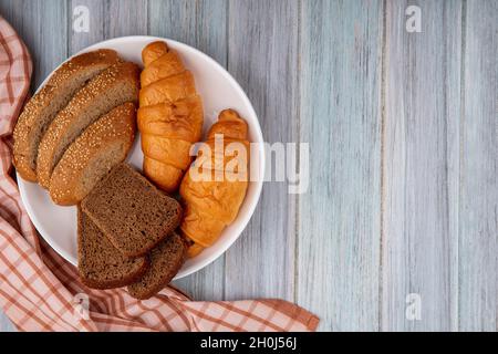 vista dall'alto di pane come croissant segale affettata e panino marrone seminato in piastra su tela di legno su sfondo con spazio copia Foto Stock