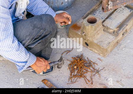 Un uomo chiodatrice è dritto vecchi chiodi arrugginiti con un martello per usarli più tardi in opere di legno Foto Stock