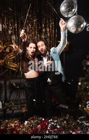 coppia entusiasta con glassatori e bicchieri da champagne per festeggiare il natale in nero Foto Stock