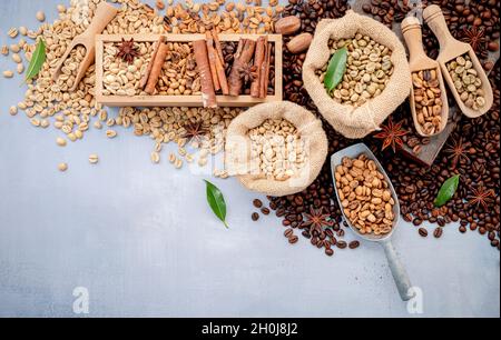 Fagioli di caffè verdi e marroni, tostati e scuri, in sacchi di canapa con sessole su fondo di cemento bianco. Foto Stock