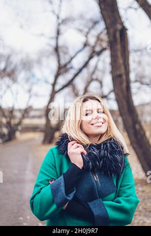 Una donna svedese attraente con un sorriso e un piacere si avvolge in un caldo e accogliente cappotto di verde all'aperto in autunno Foto Stock