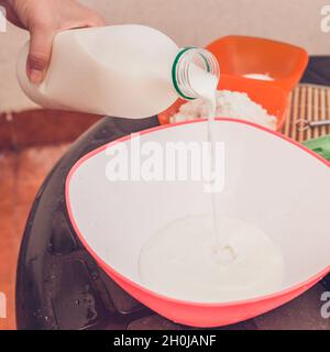 Aggiungere alla massa dell'uovo una piccola parte del latte, da qualche parte 100-150 ml - non versiamo tutto il latte in una volta, perché quando si aggiunge la farina, l'impasto più spesso è Foto Stock