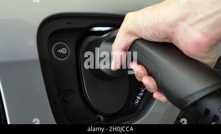 Primo piano di una mano inserendo un caricabatterie elettrico nella presa di una vettura elettrica grigia Foto Stock