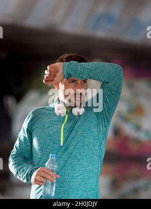 Uomo stanco che pulendo il sudore dalla fronte e tenendo la bottiglia d'acqua dopo l'allenamento Foto Stock