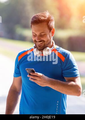 Sorridente bell'uomo che guarda il cellulare dopo la ricreazione nel parco Foto Stock