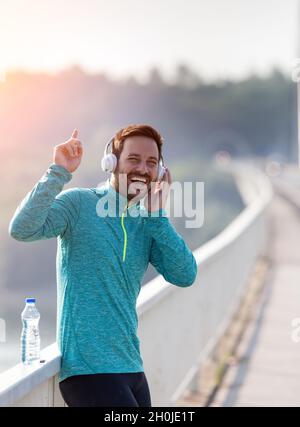 L'uomo felice ascolta la musica sulle cuffie dopo aver fatto jogging sul ponte Foto Stock