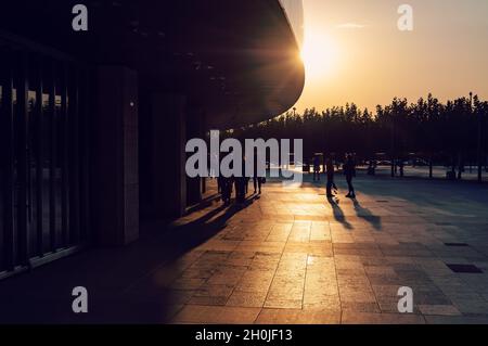 Gruppo di persone al tramonto estivo sulla strada piastrellata nel parco cittadino Foto Stock