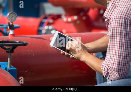 Primo piano delle mani dell'ingegnere con il tablet davanti alla pipeline in un impianto all'aperto Foto Stock