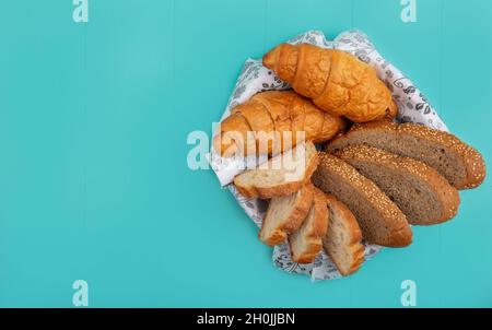 vista dall'alto del pane come baguette di pannocino seminato e croissant in ciotola su sfondo blu con spazio copia Foto Stock