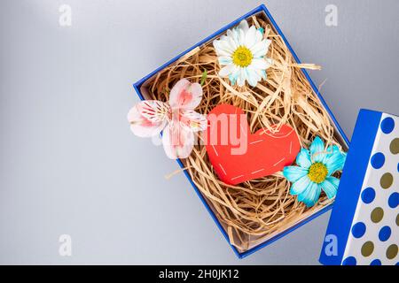 vista dall'alto di colorati fiori a margherita e di un'allstroemeria rosa con un cuore di carta rossa e con paglia in una scatola blu presente su sfondo bianco Foto Stock