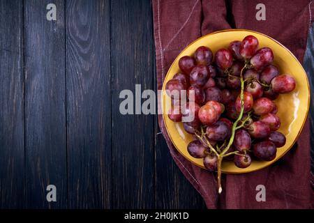 vista dall'alto dell'uva dolce fresca in un piatto su sfondo di legno scuro con spazio copia Foto Stock