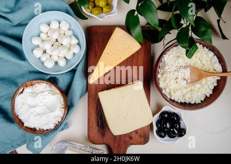 vista dall'alto di diversi tipi di formaggio su tagliere di legno e formaggio caserario in una ciotola di legno con olive sottaceto su sfondo rustico Foto Stock