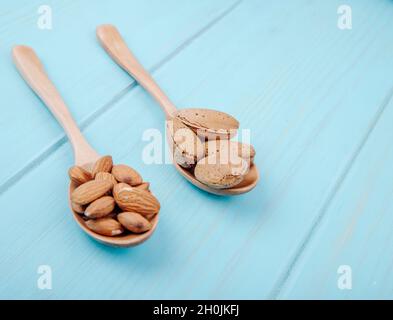 vista laterale di cucchiai di legno con mandorla in guscio e senza guscio su sfondo di legno blu Foto Stock